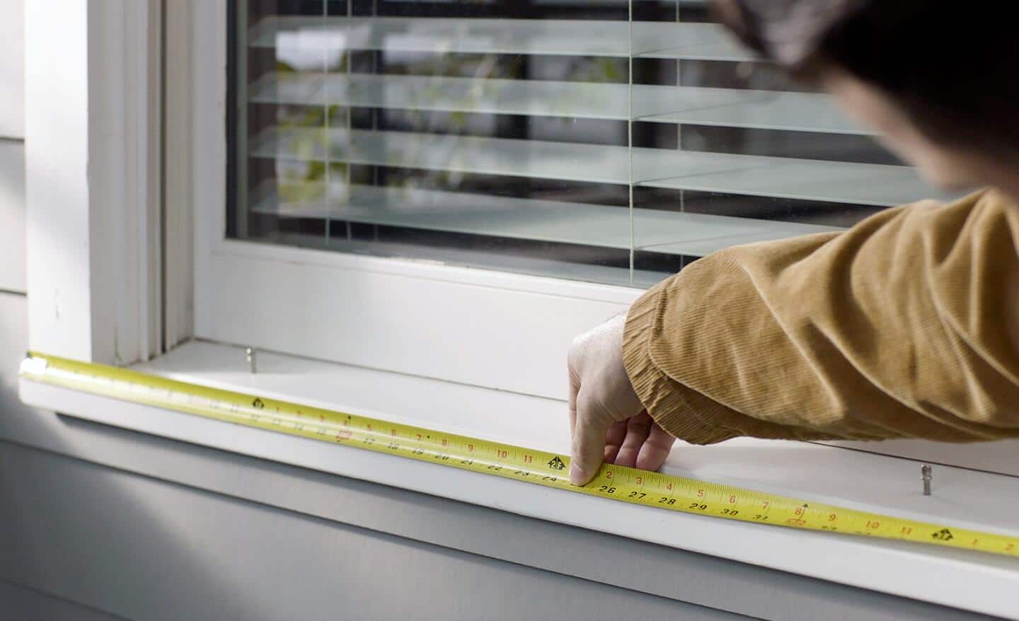 Person using a measuring tape on a windowsill to hang Christmas lights. Person using a measuring tape on a windowsill to hang Christmas lights.