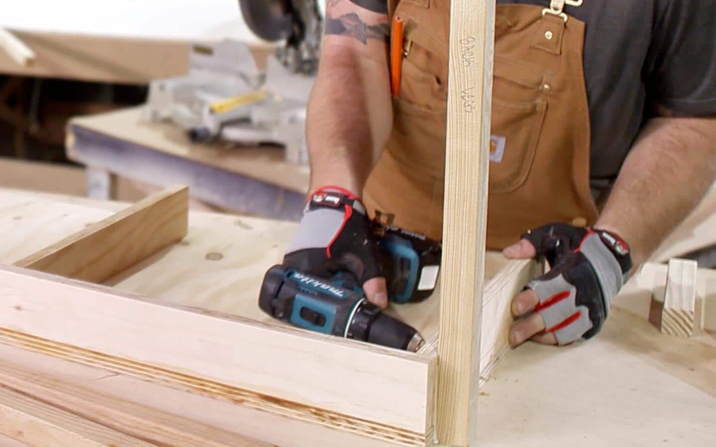 A cordless drill makes freehand pocket holes near the corner of a wooden box of a DIY desk.