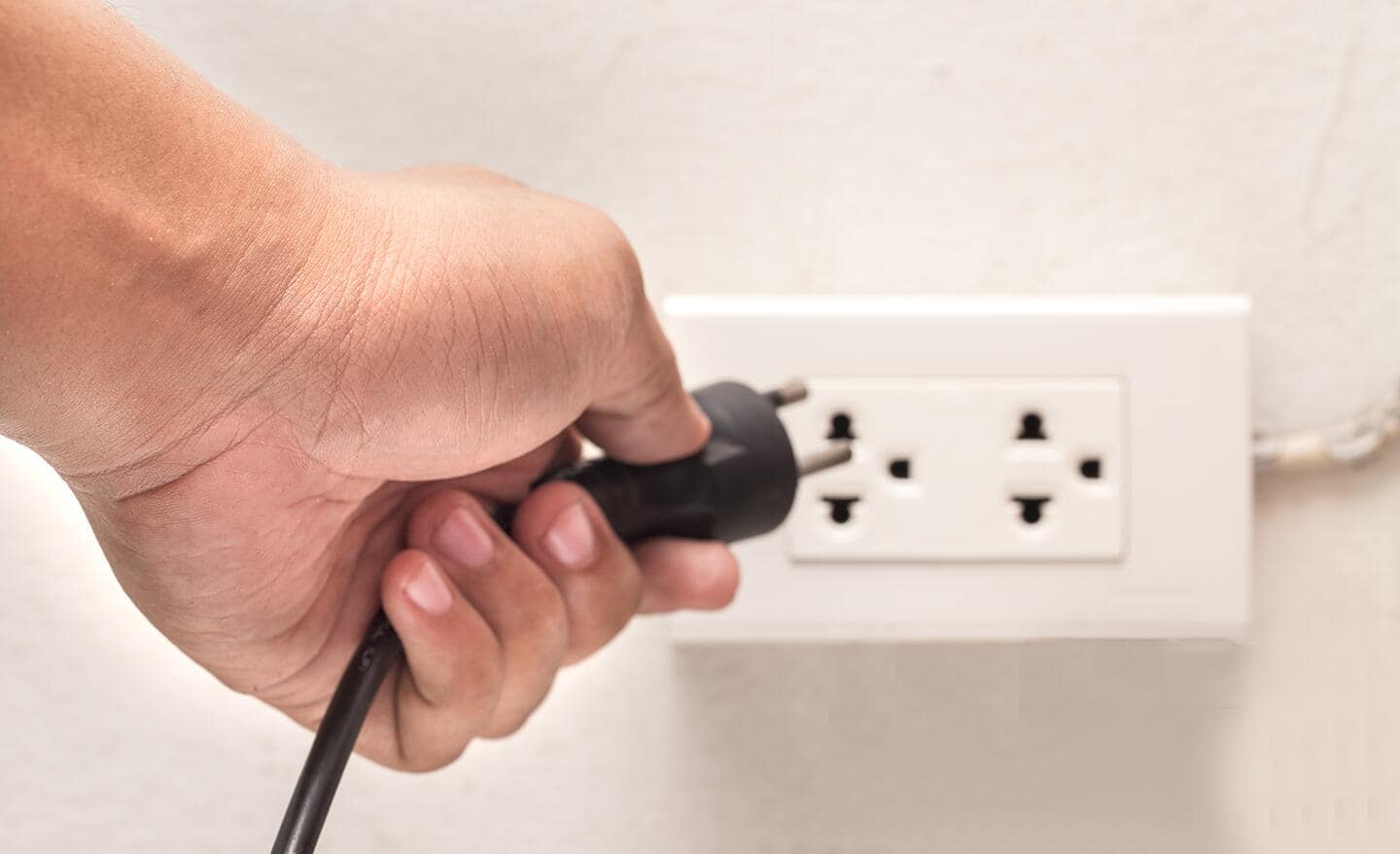 A person unplugs a refrigerator from a wall socket.