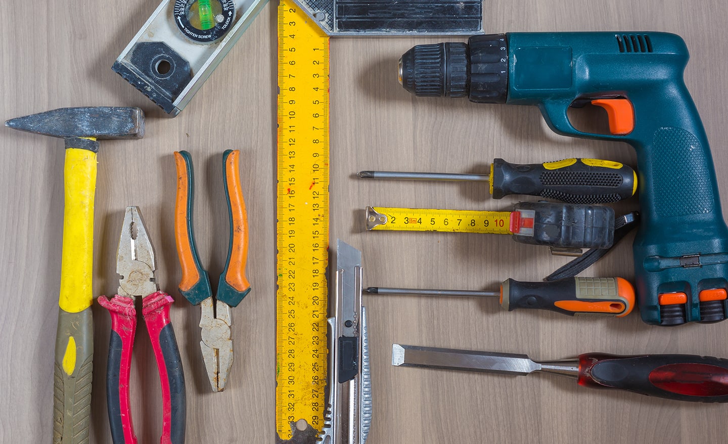 A hammer, measuring tape, drill and other tools laid out on a table.