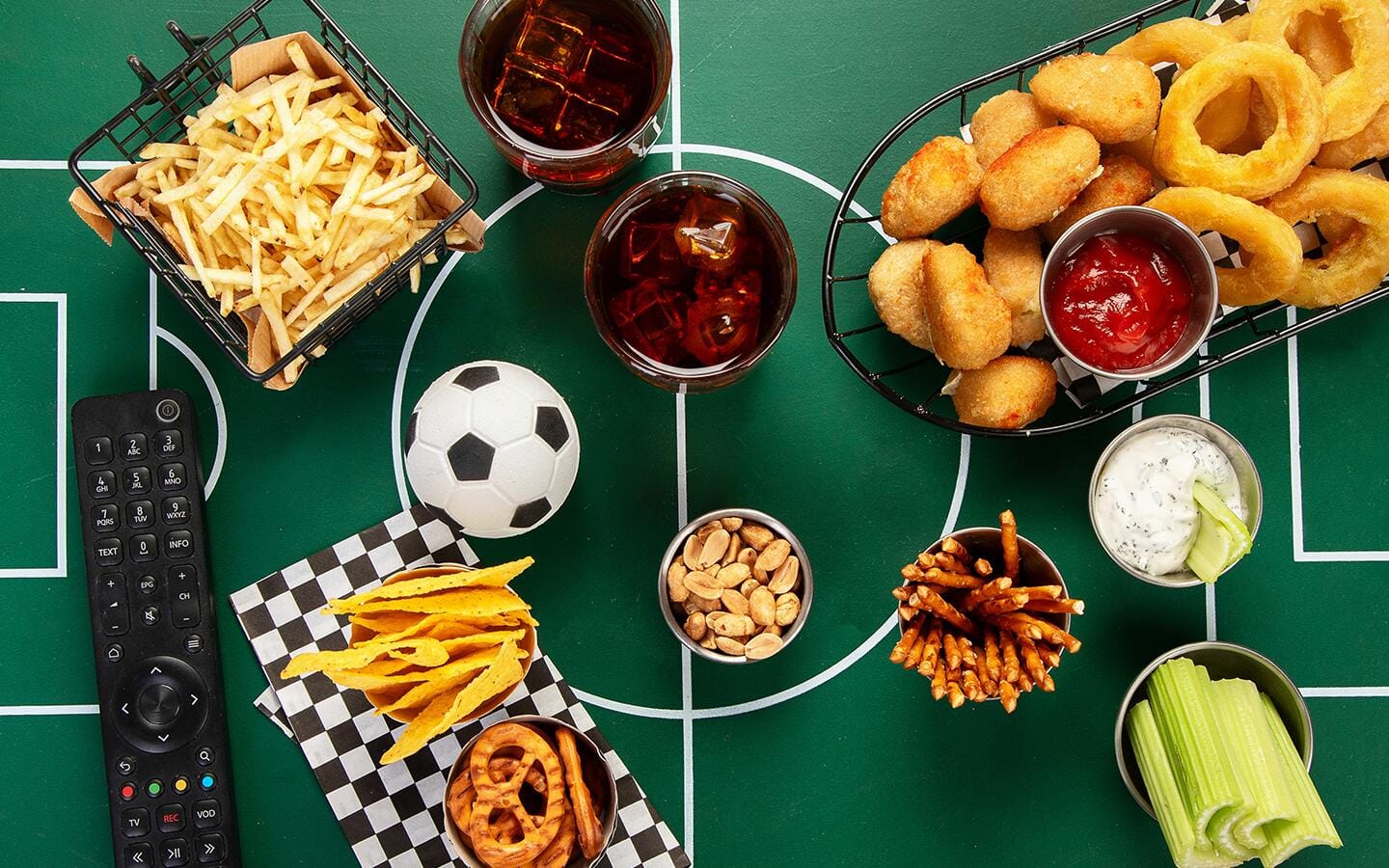 A game day spread on a soccer-themed tablecloth that features party finger foods and drinks. A game day spread on a soccer-themed tablecloth that features party finger foods and drinks.