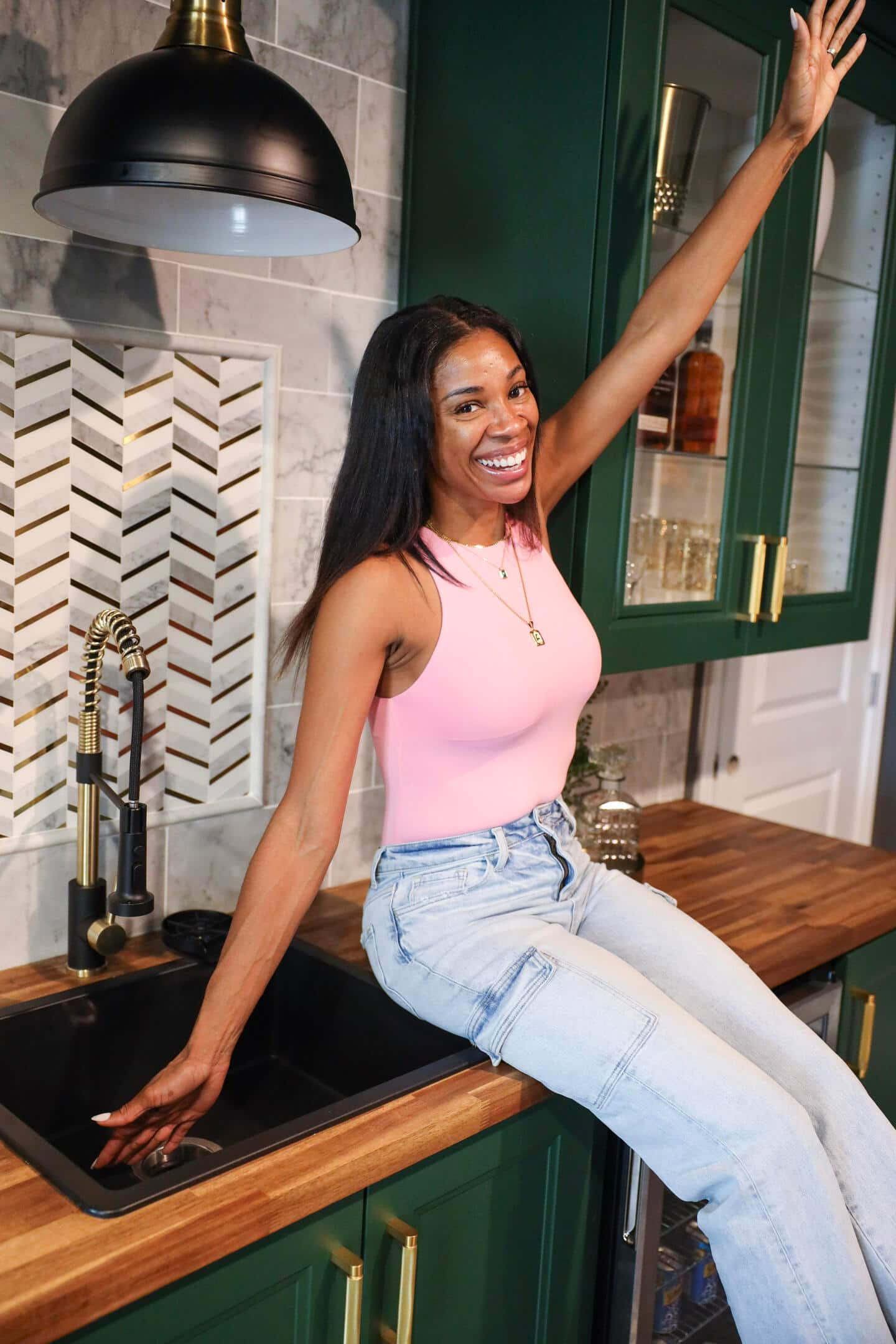 Woman sitting on top of a completed bar area with butcherblock countertops and green cabinets