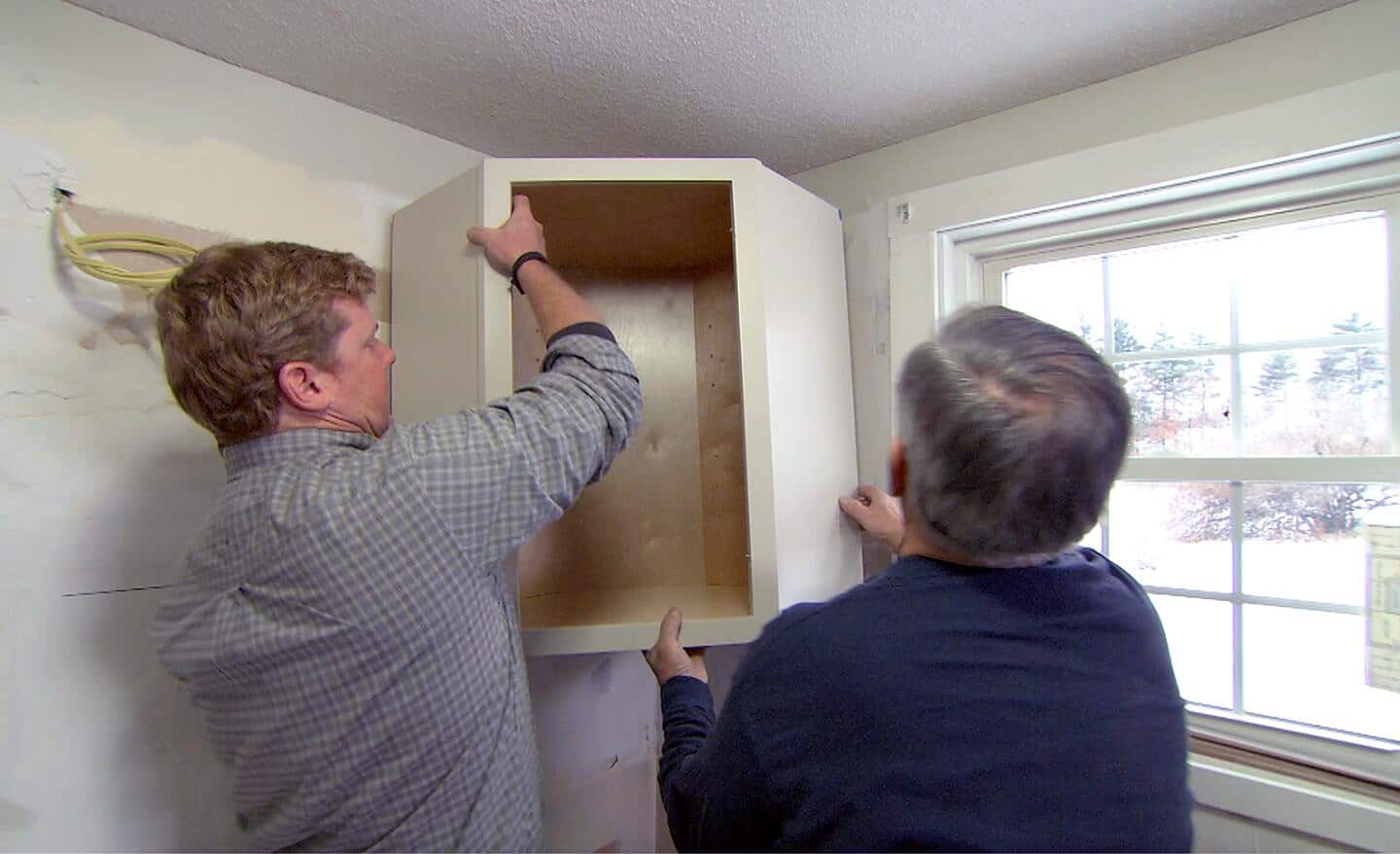 A person installs a corner cabinet with the assistance of a helper.