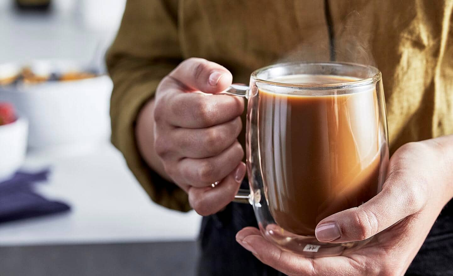 A person holds a glass mug full of coffee. A person holds a glass mug full of coffee.