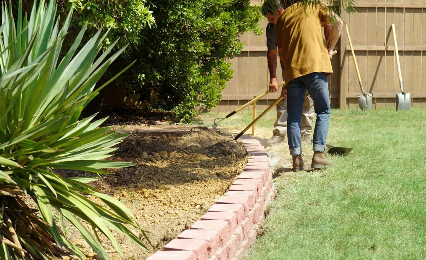 Two men leveling the fill dirt behind a new retaining wall.