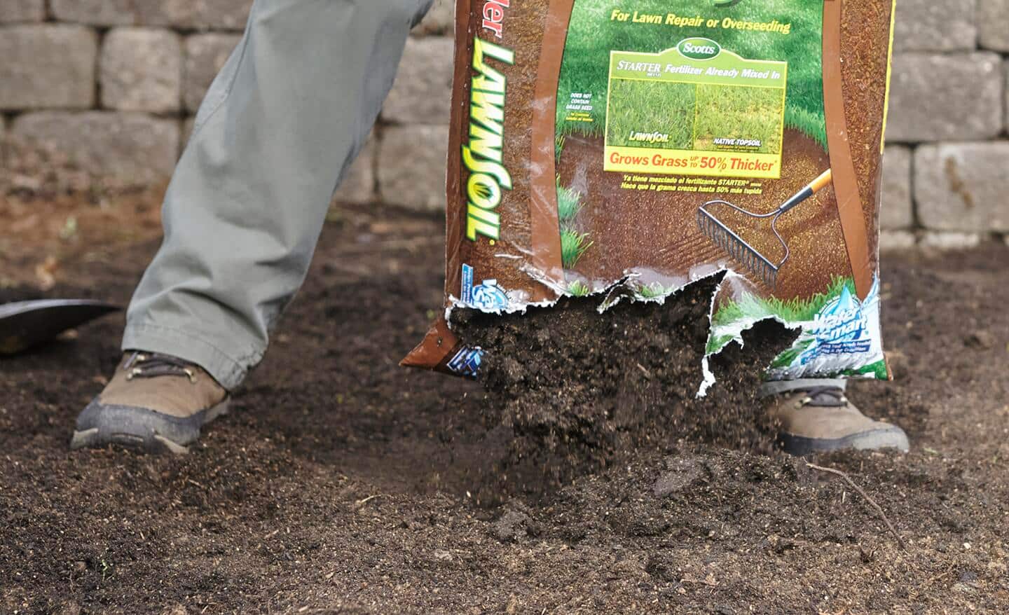 A person adds topsoil to a shallow hole in outdoor soil.