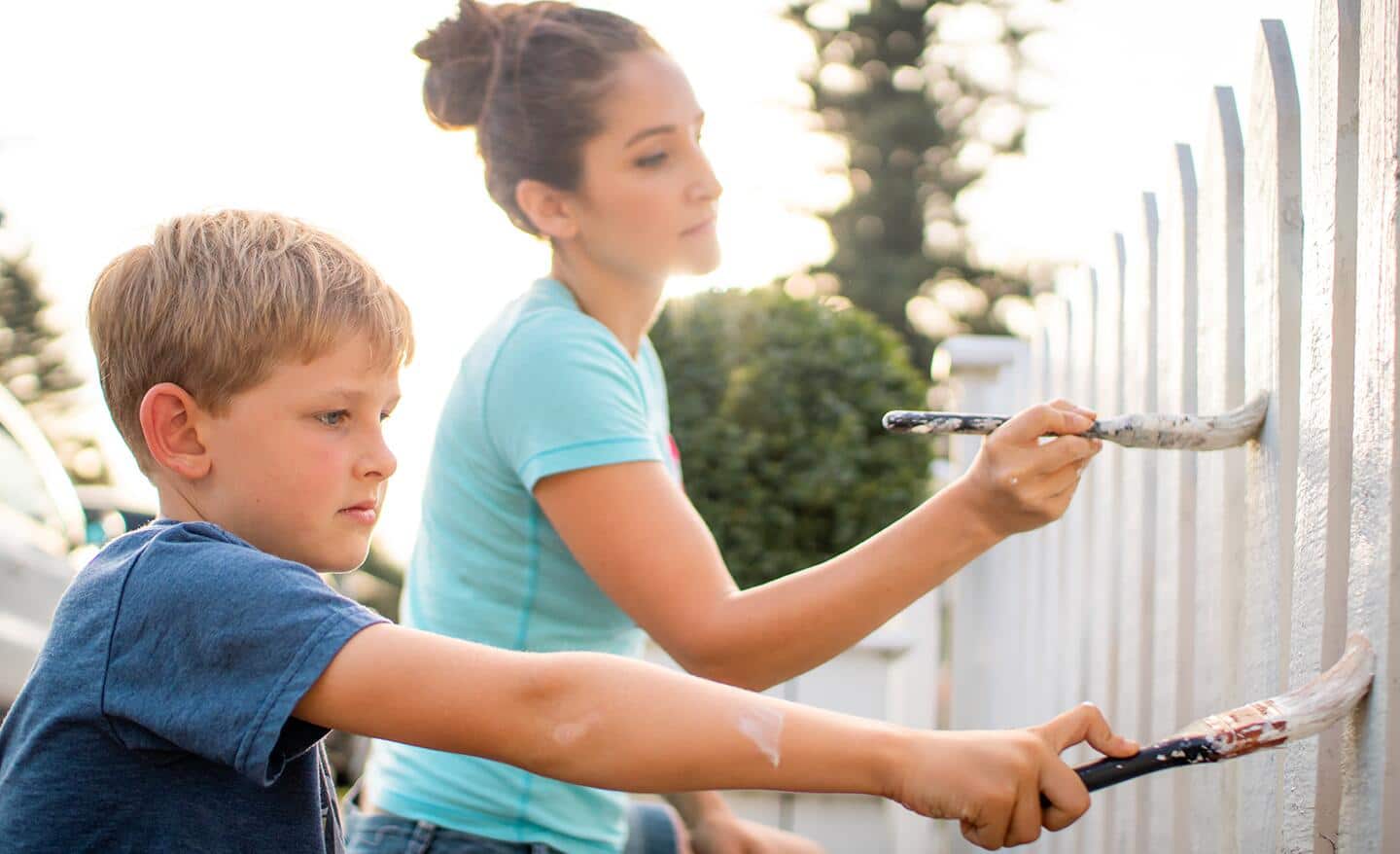 A woman and child painting a fence white. A woman and child painting a fence white.