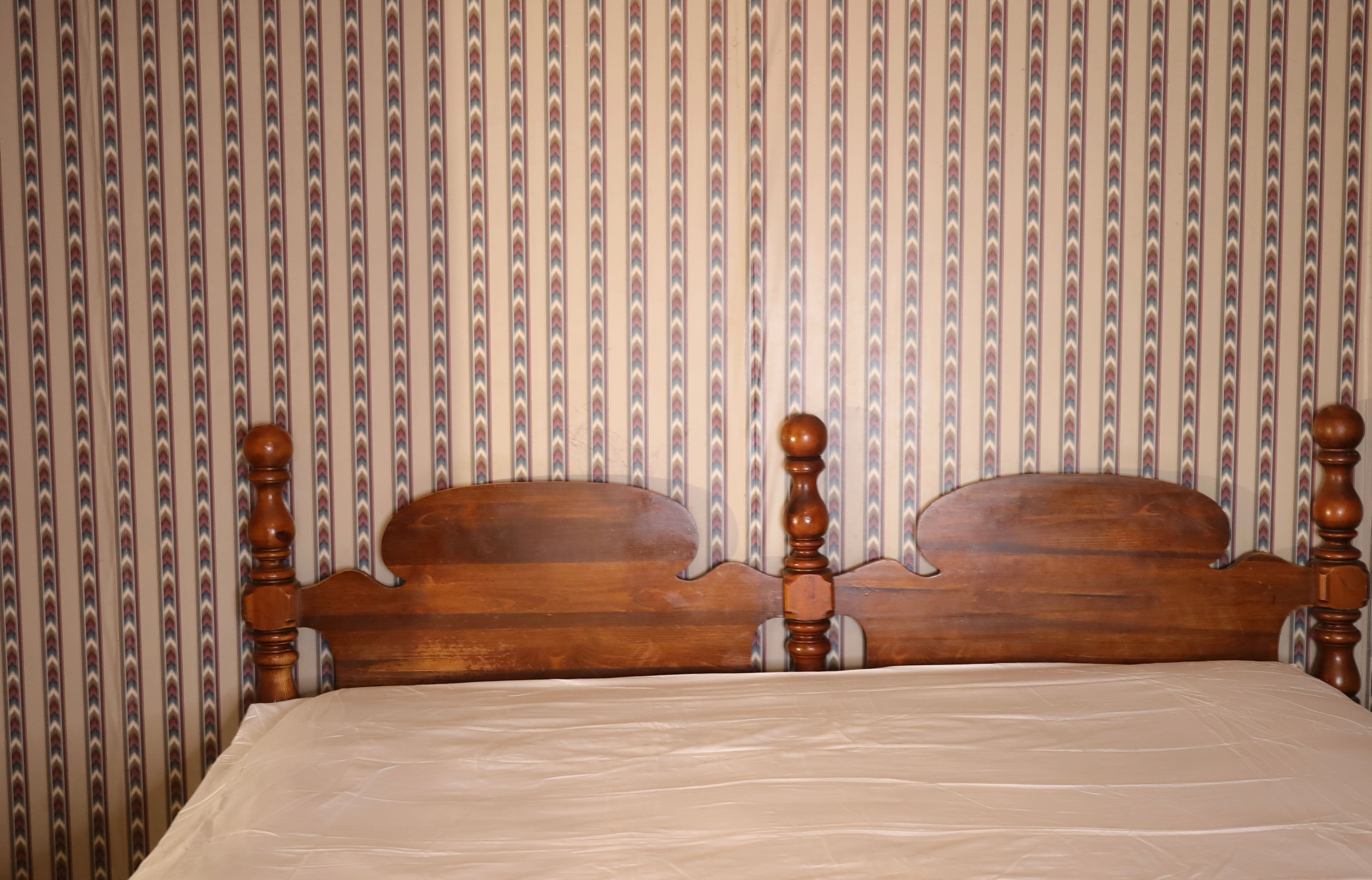 Before photo of a bedroom with brown patterned wallpaper and a wooden headboard.