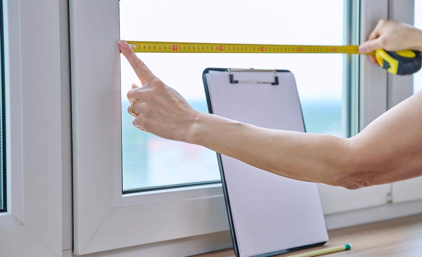 A person measures a window's width using a tape measure.