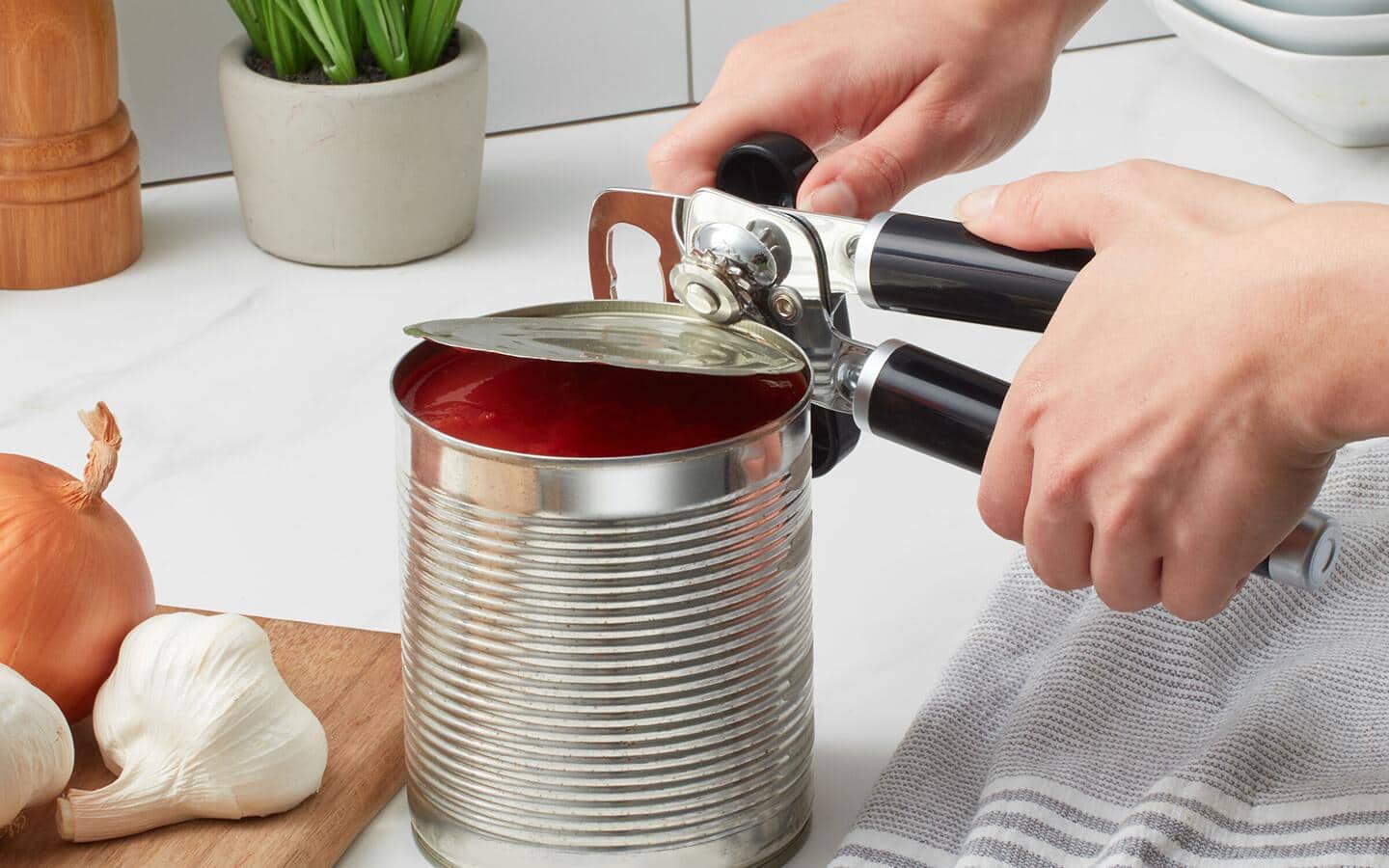 Someone using a handheld can opener to open a can. Someone using a handheld can opener to open a can.