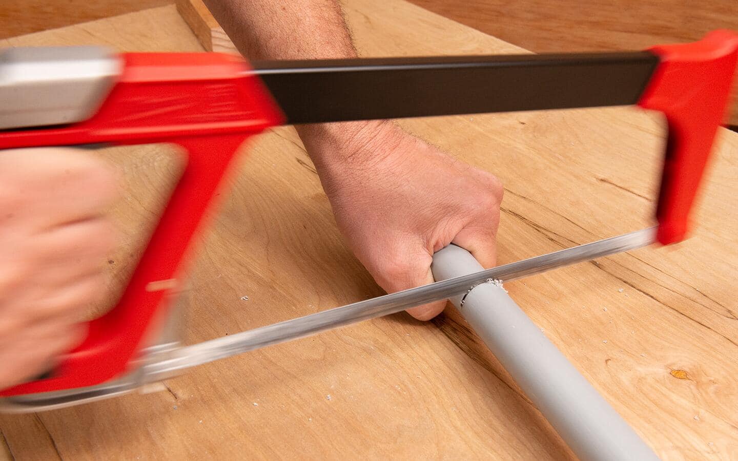 A person cutting conduit with a hacksaw. 