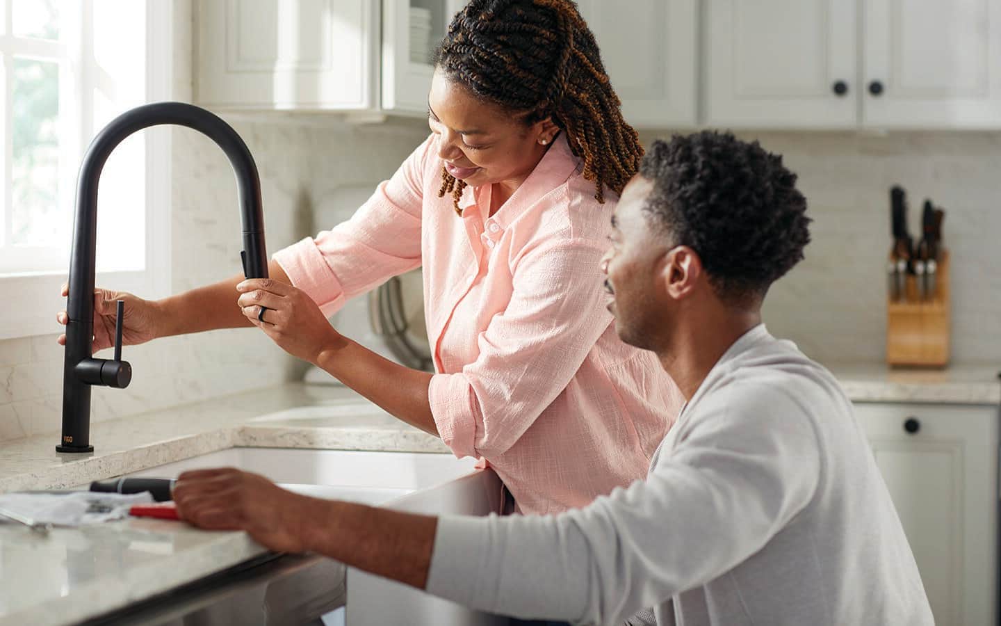 A couple installing a new black kitchen faucet.