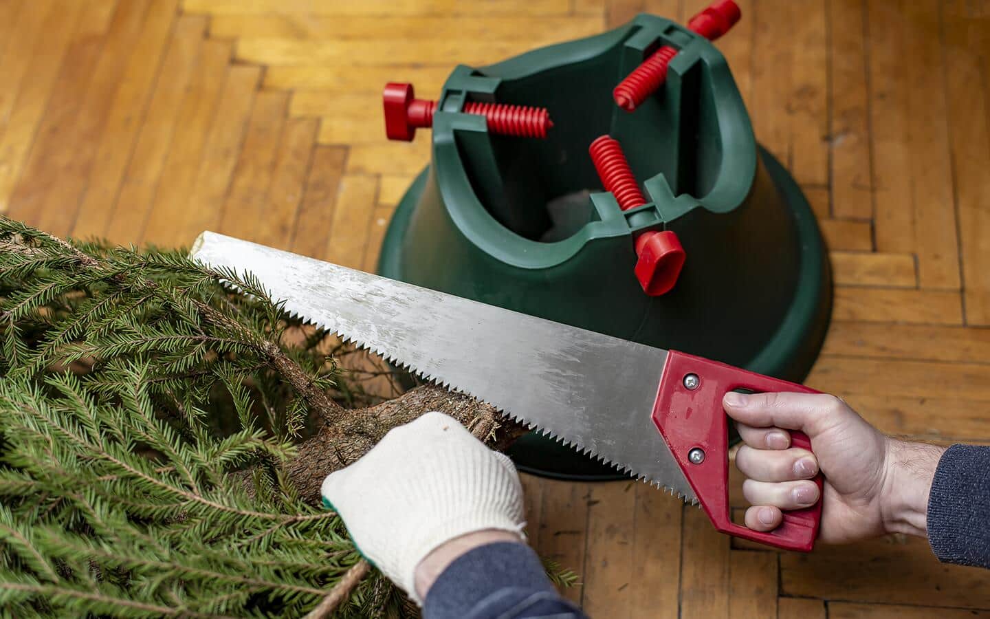 A person uses a saw to trim a Christmas tree's trunk.  A person uses a saw to trim a Christmas tree's trunk.