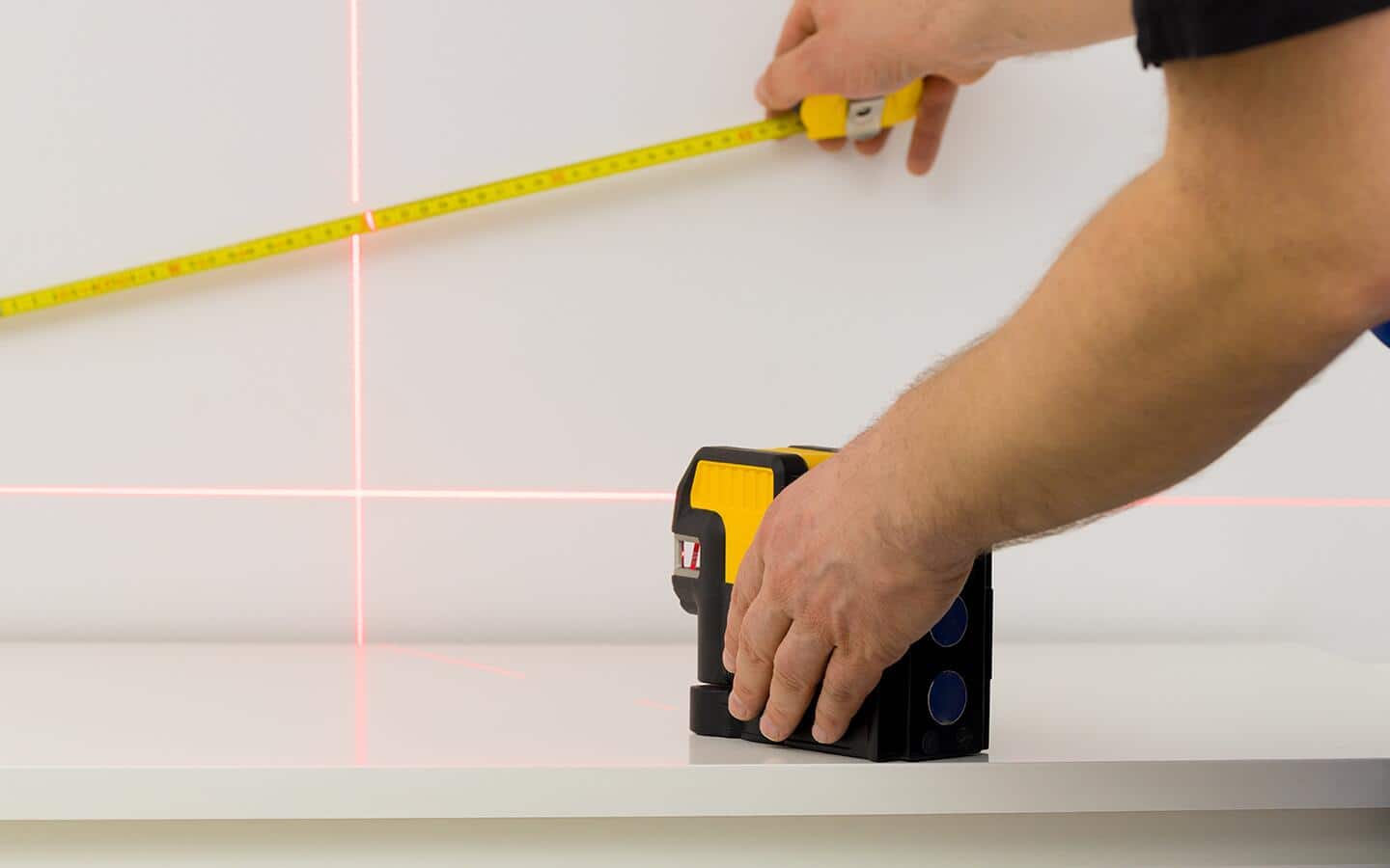 A person using a laser-guided level on a wall. A person using a laser-guided level on a wall.