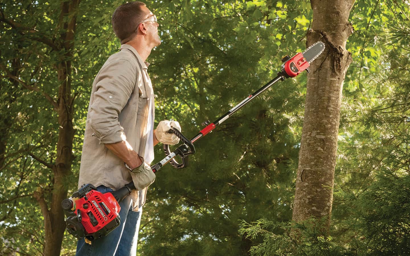A person wearing safety equipment uses a gas pole saw to cut tree limbs.