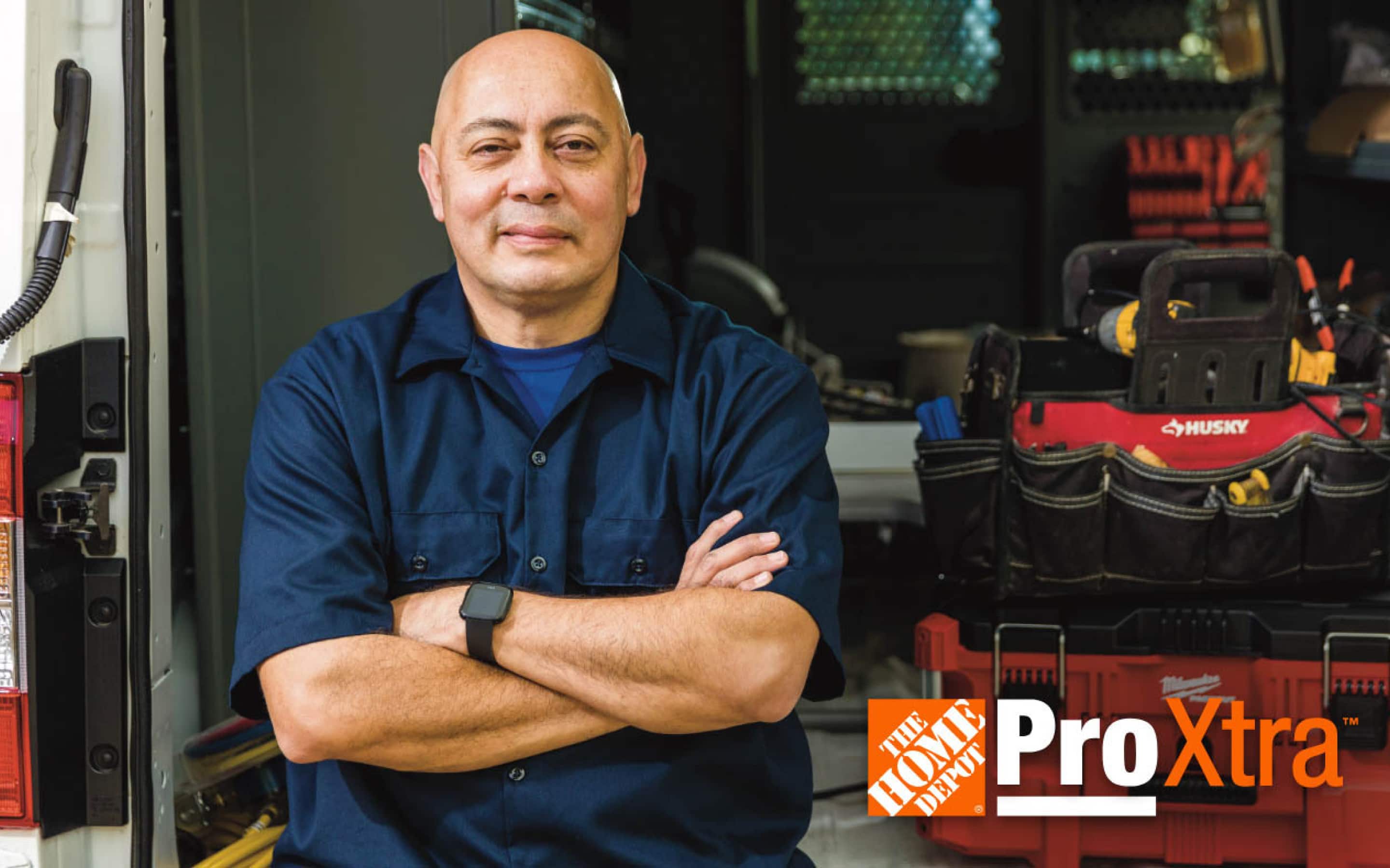 Un contratista con los brazos cruzados recargado en su camioneta de trabajo con herramientas y el logotipo de Pro Xtra de The Home Depot.
