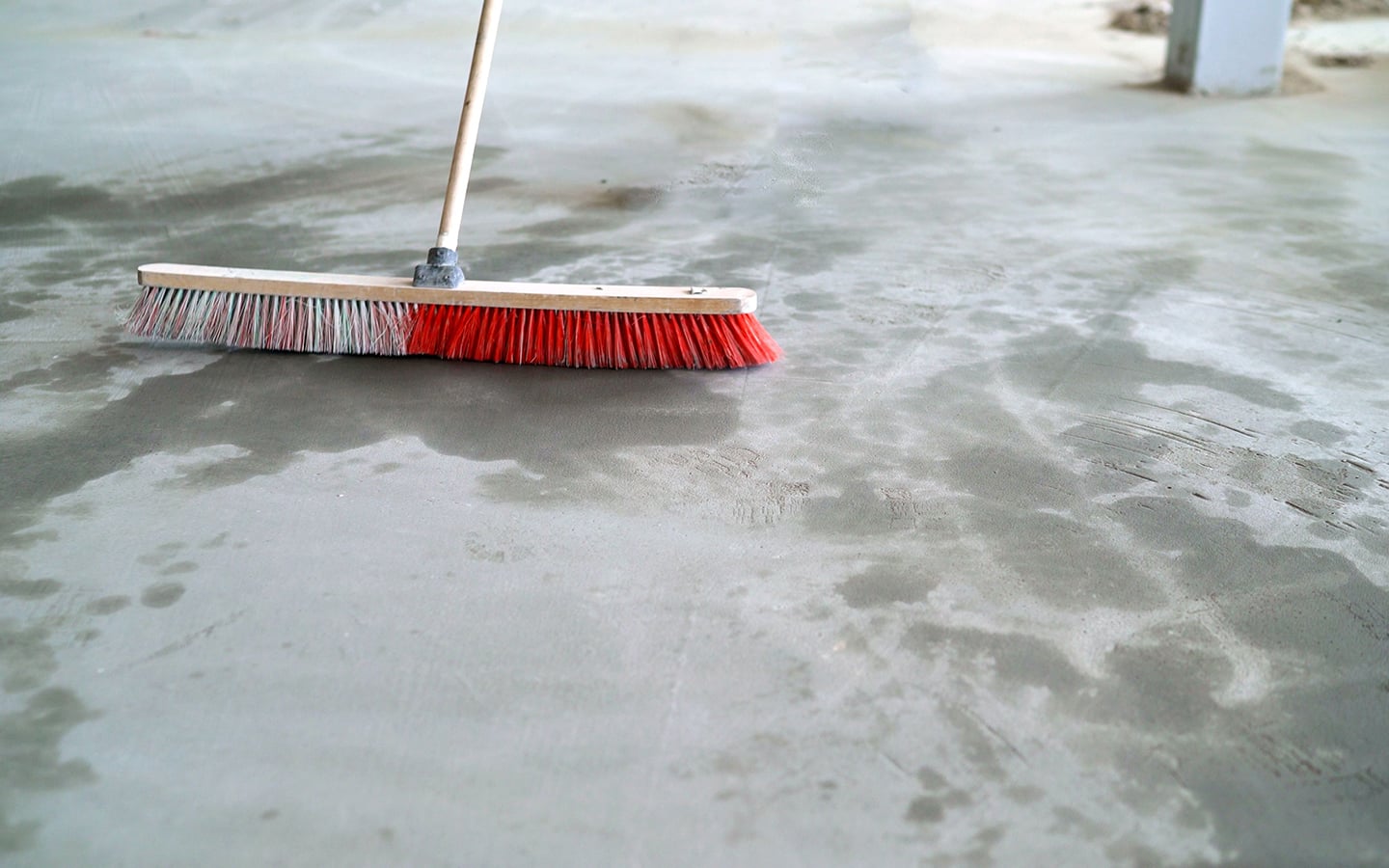 Someone using a push broom to sweep a concrete floor.