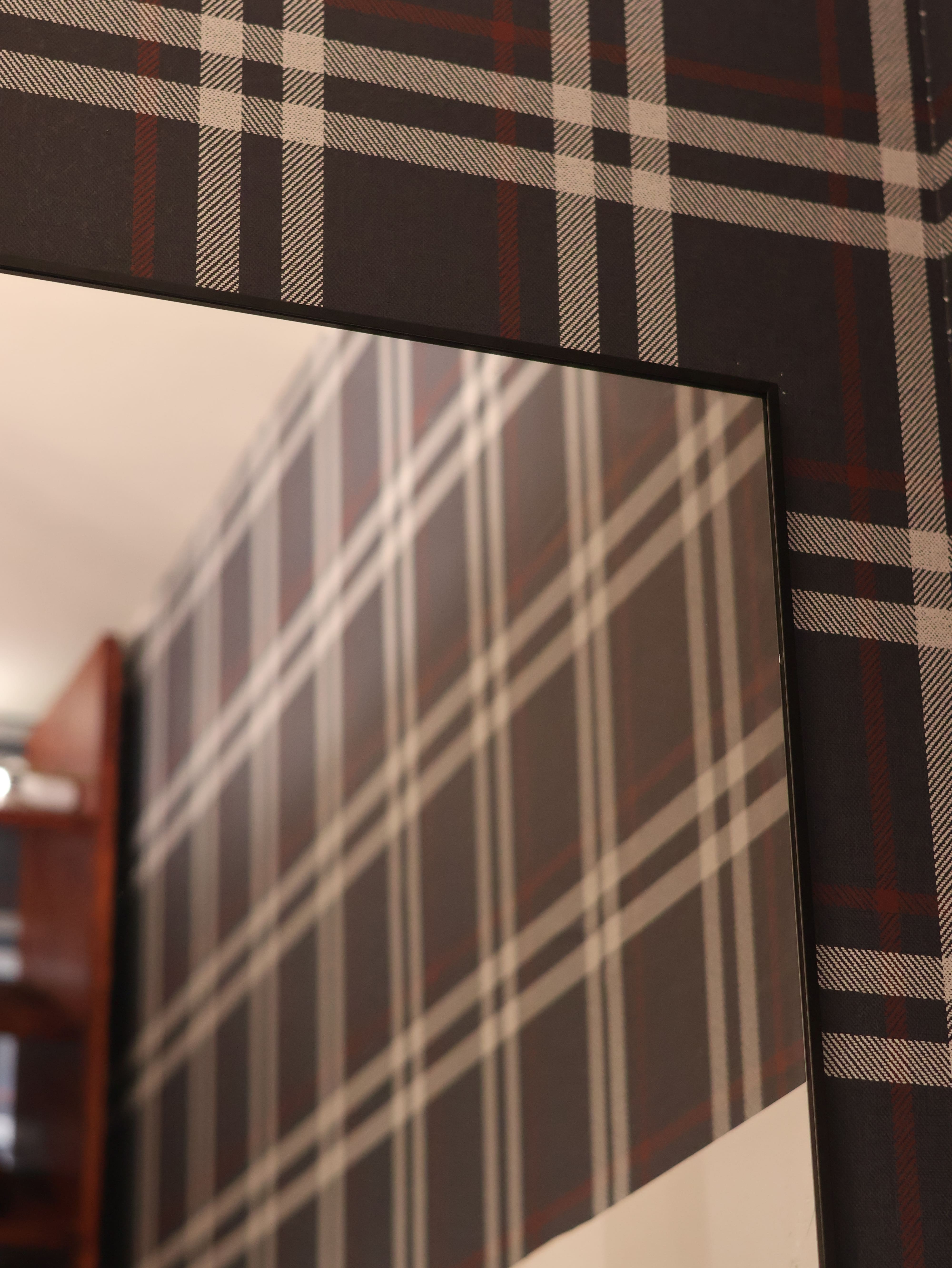 Close-up shot of a mirror installed in a newly renovated closet featuring plaid wallpaper.