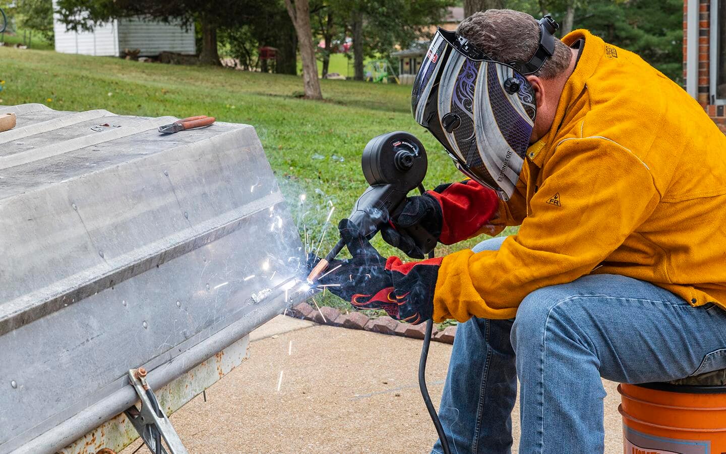 A person in special welding safety gear, including a helmet, jacket and gloves, welding metal outdoors.