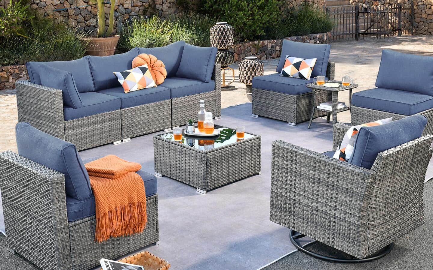 A wicker patio set comprised of a sofa and chairs, with various cushions and blankets, and a matching table. 
