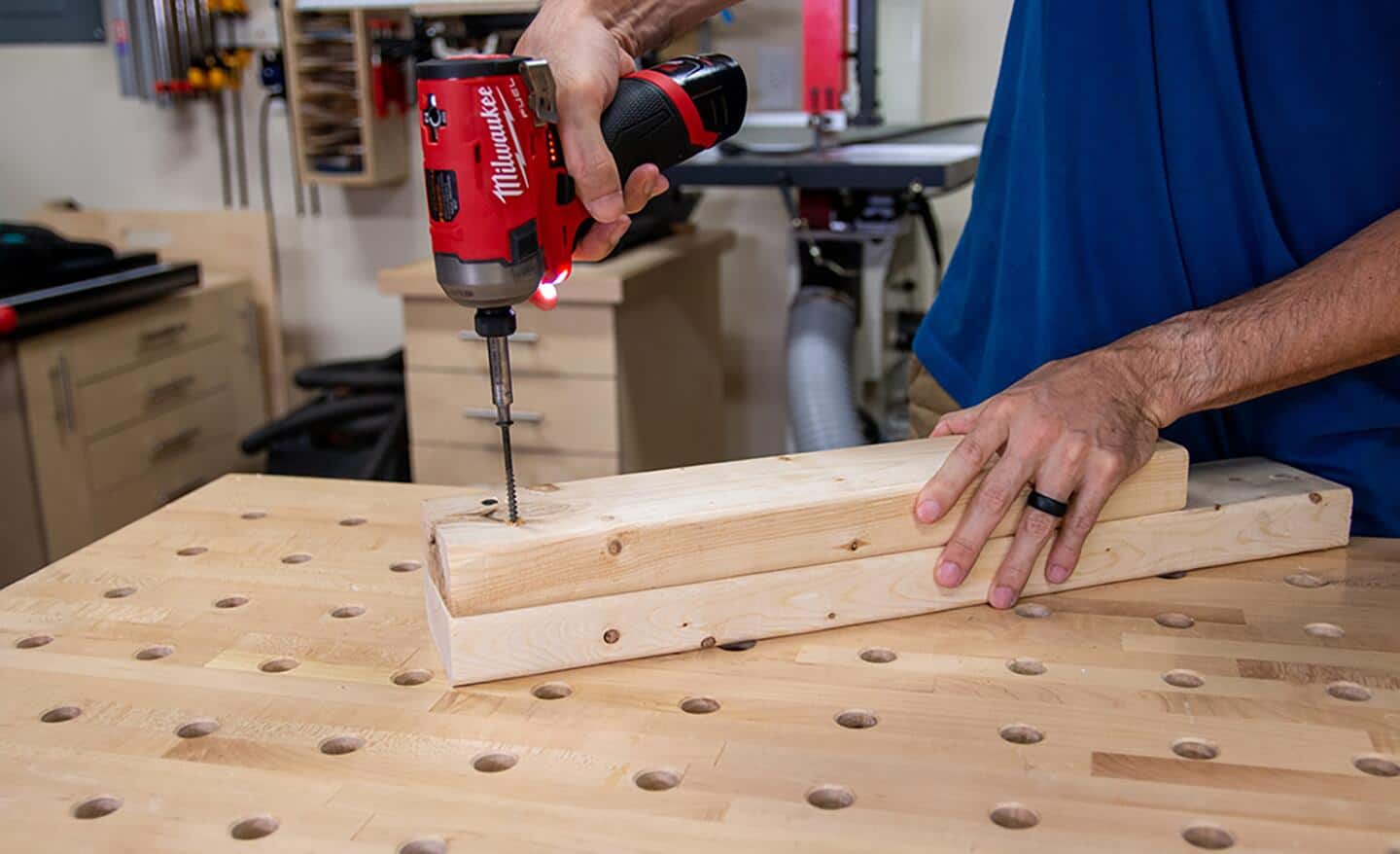 Someone using a hammer drill on two wood boards.