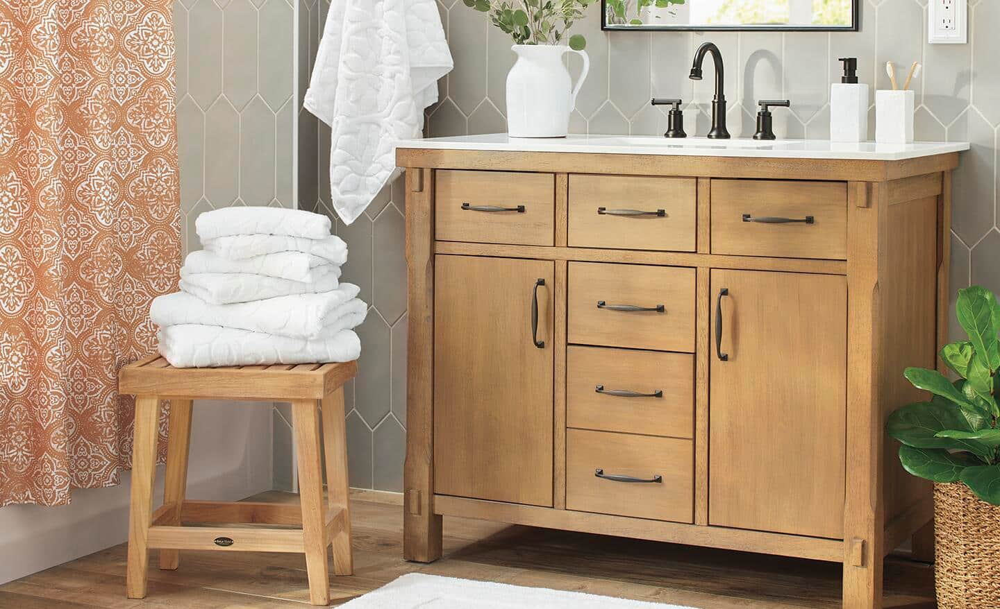 White towels stacked on a stool in a bathroom with complementary accessories on the cabinet.