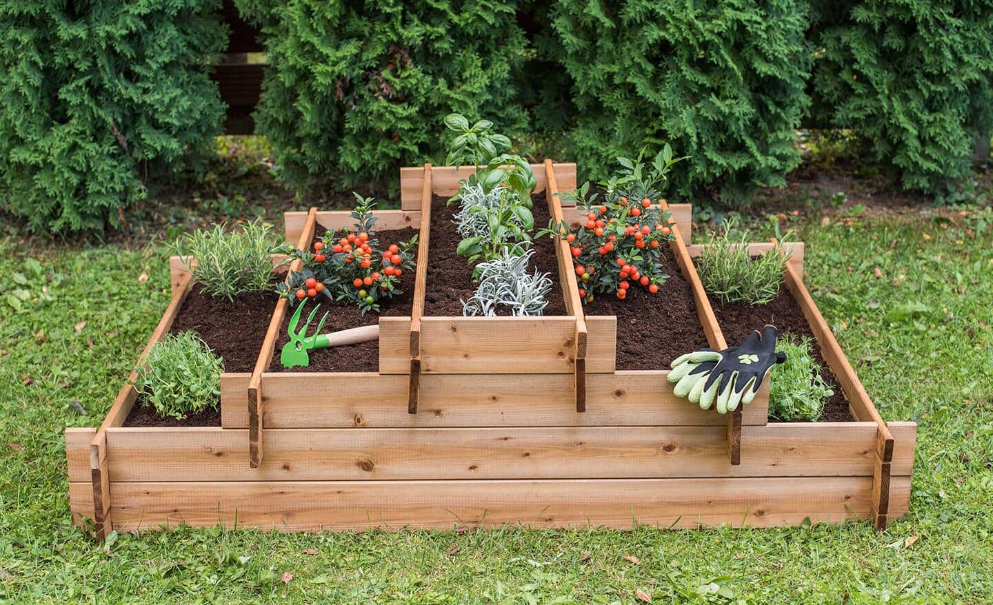 A wooden multi-tiered raised garden bed full of flowers sitting on grass in a yard. 