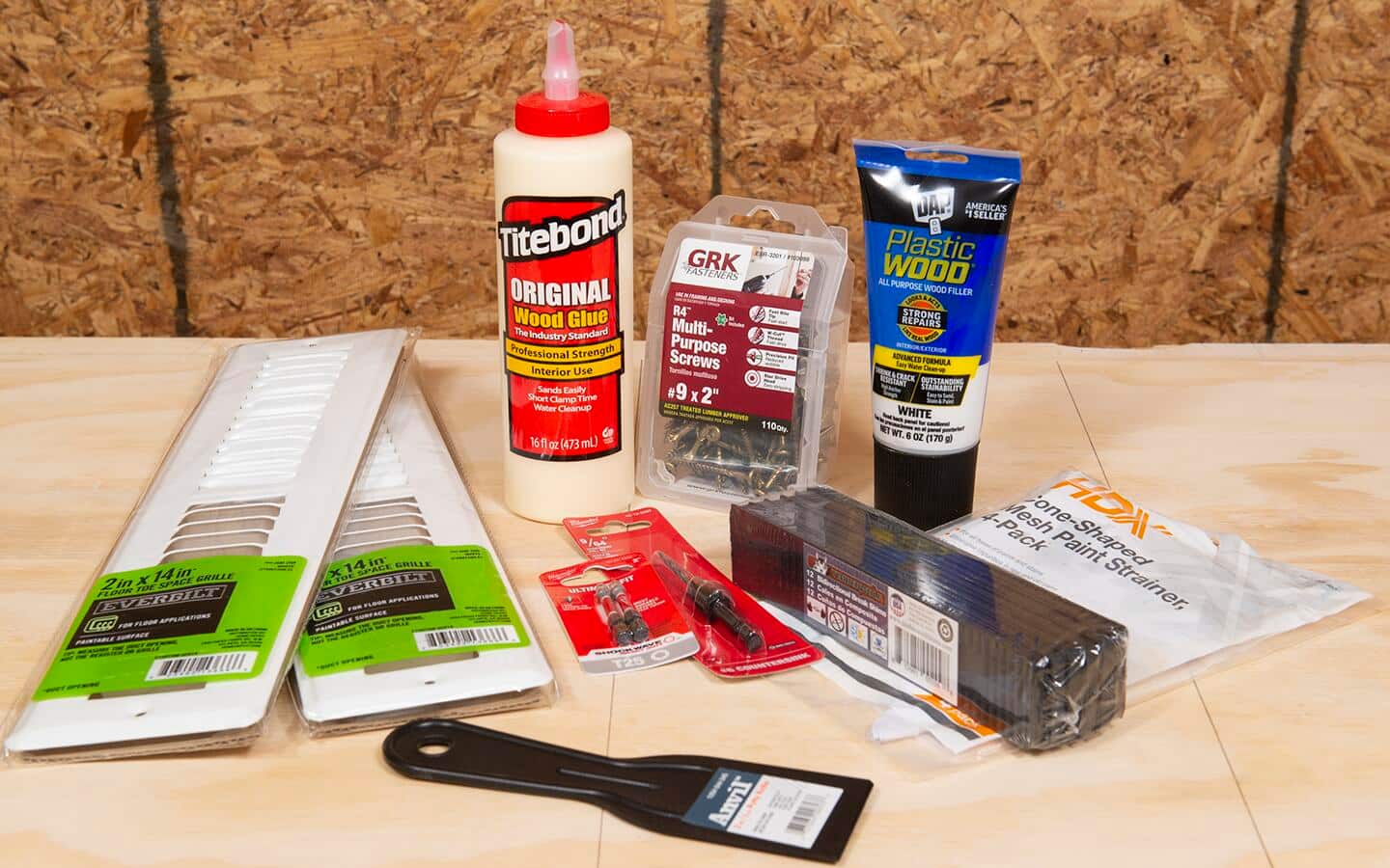 An assortment of building materials, including vent covers, a putty knife, countersunk drill bit, screwdriver bit, screws, plastic shims, paint filters and wood filler.