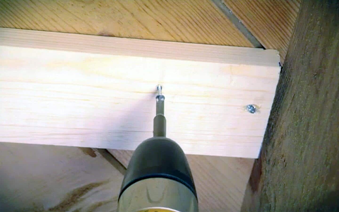 A person drilling screws below a subfloor into the hardwood floor above.