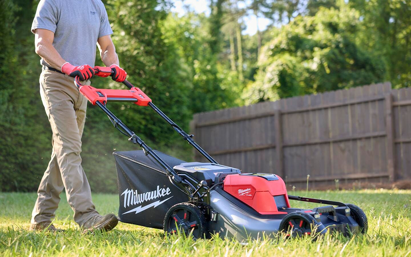 A person wearing work gloves pushes a lawn mower on a lawn.