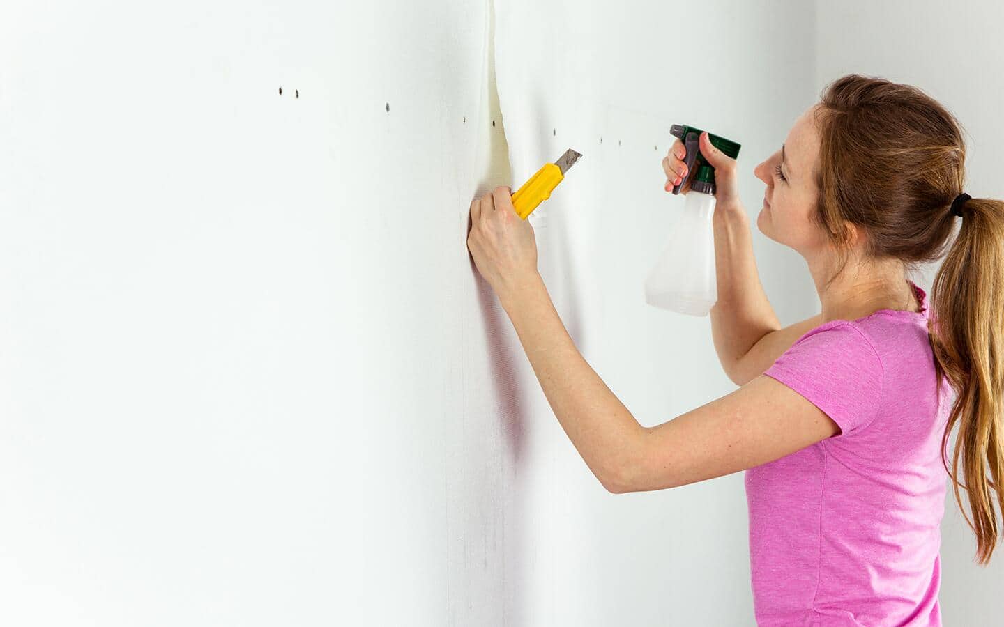 A person applies gel wallpaper remover with a spray bottle. A person applies gel wallpaper remover with a spray bottle.