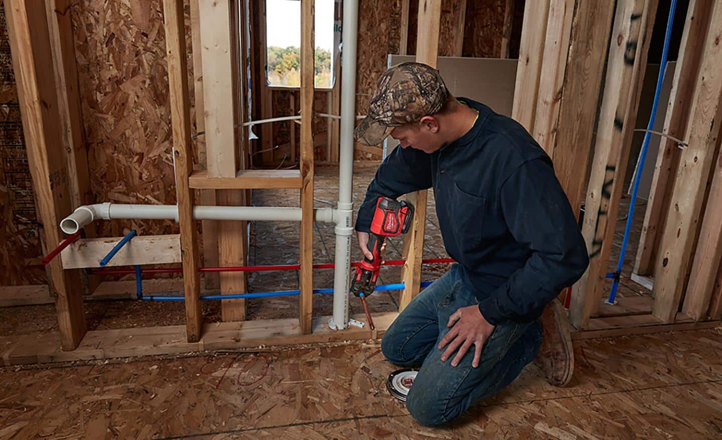 A plumber uses a battery powered crimping tool to join PEX pipes in a house under construction.