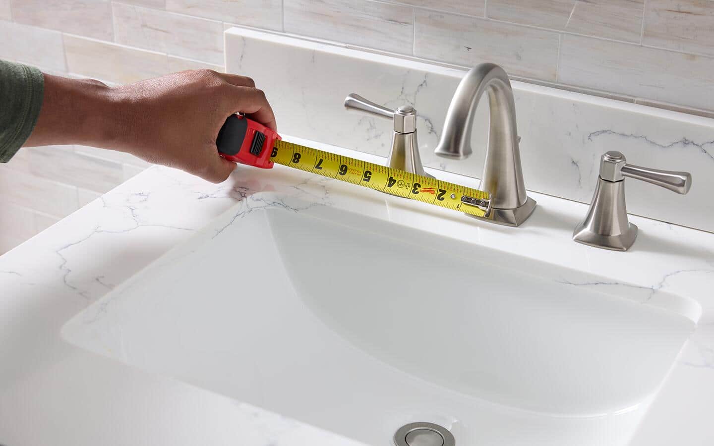 A tape measure is used to determine the width of a widespread bathroom faucet.