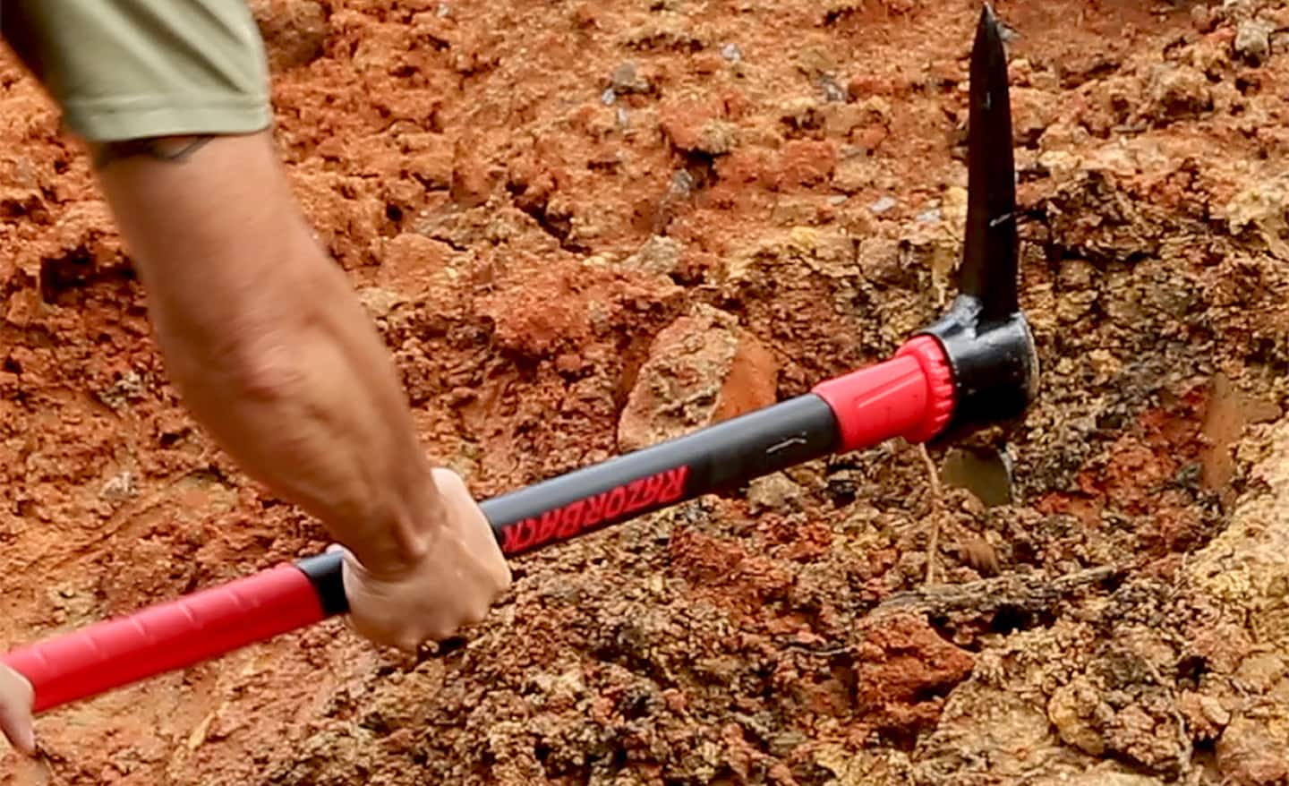 A person uses a pick axe to dig in dirt.
