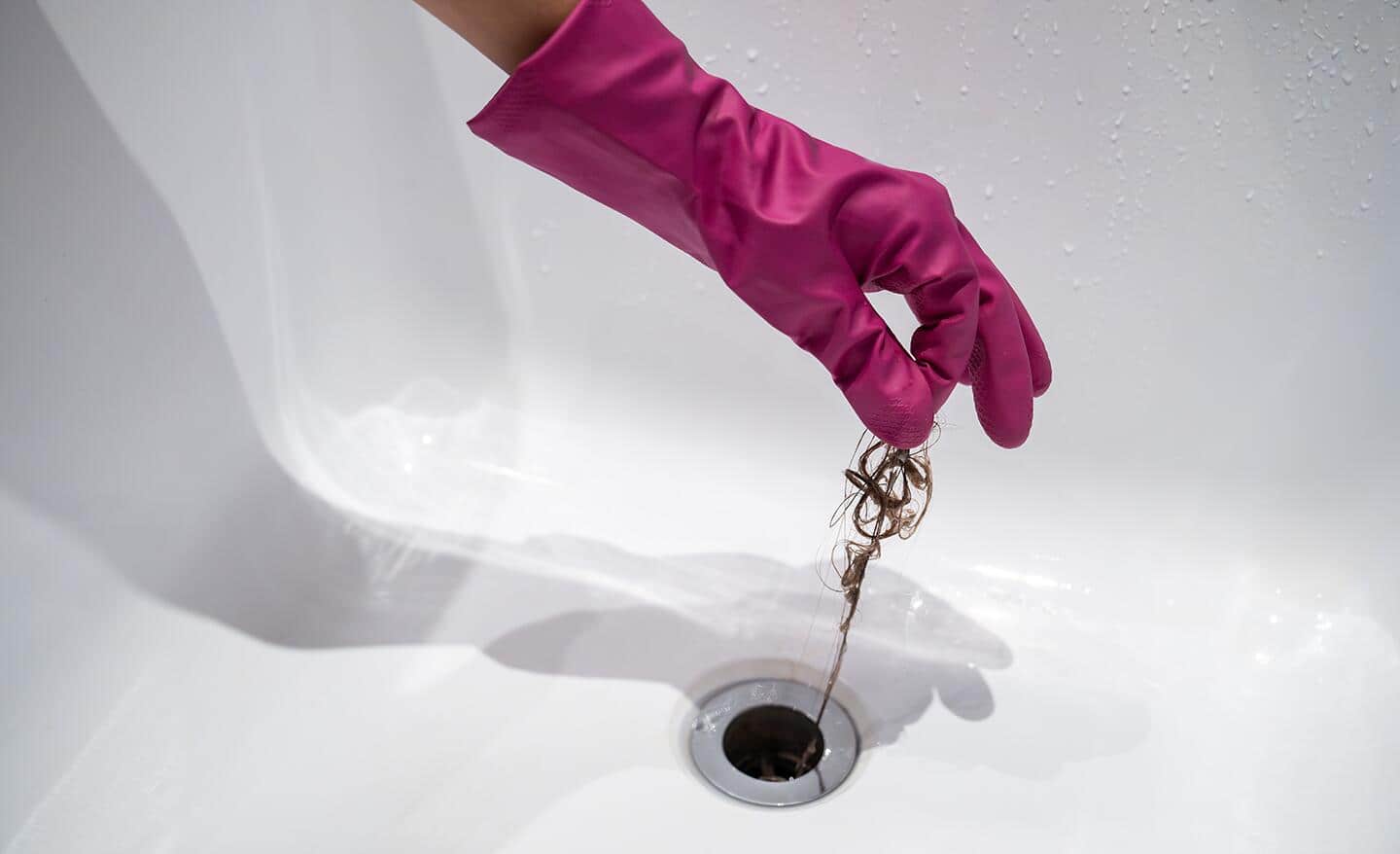 A gloved hand pulls hair from a drain.