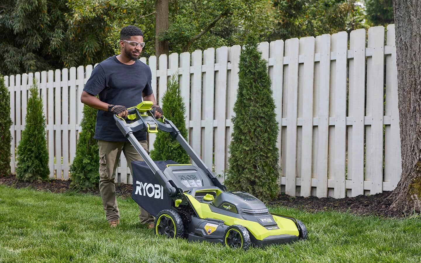 A person wearing safety glasses mows the lawn in a yard. A person wearing safety glasses mows the lawn in a yard.