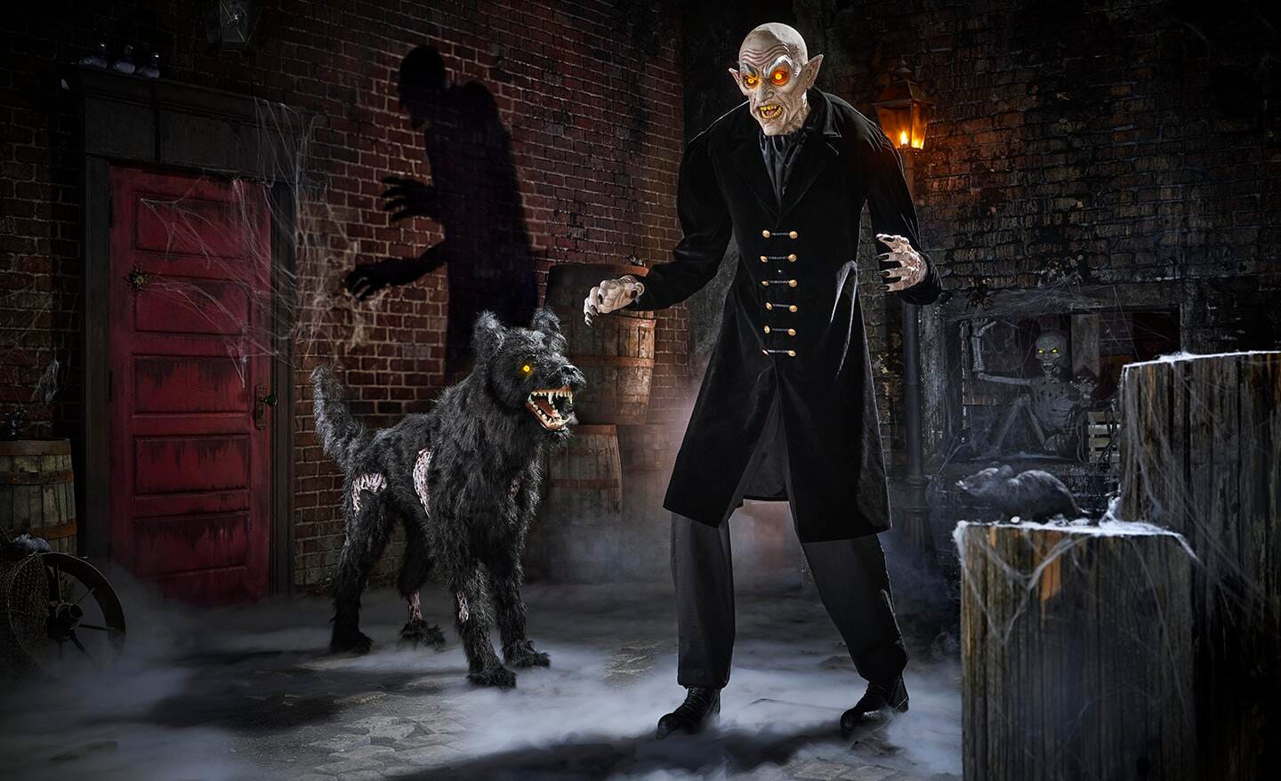 An animatronic vampire with eyes that glow stands in the center of a scary scene in a courtyard decorated for Halloween. 