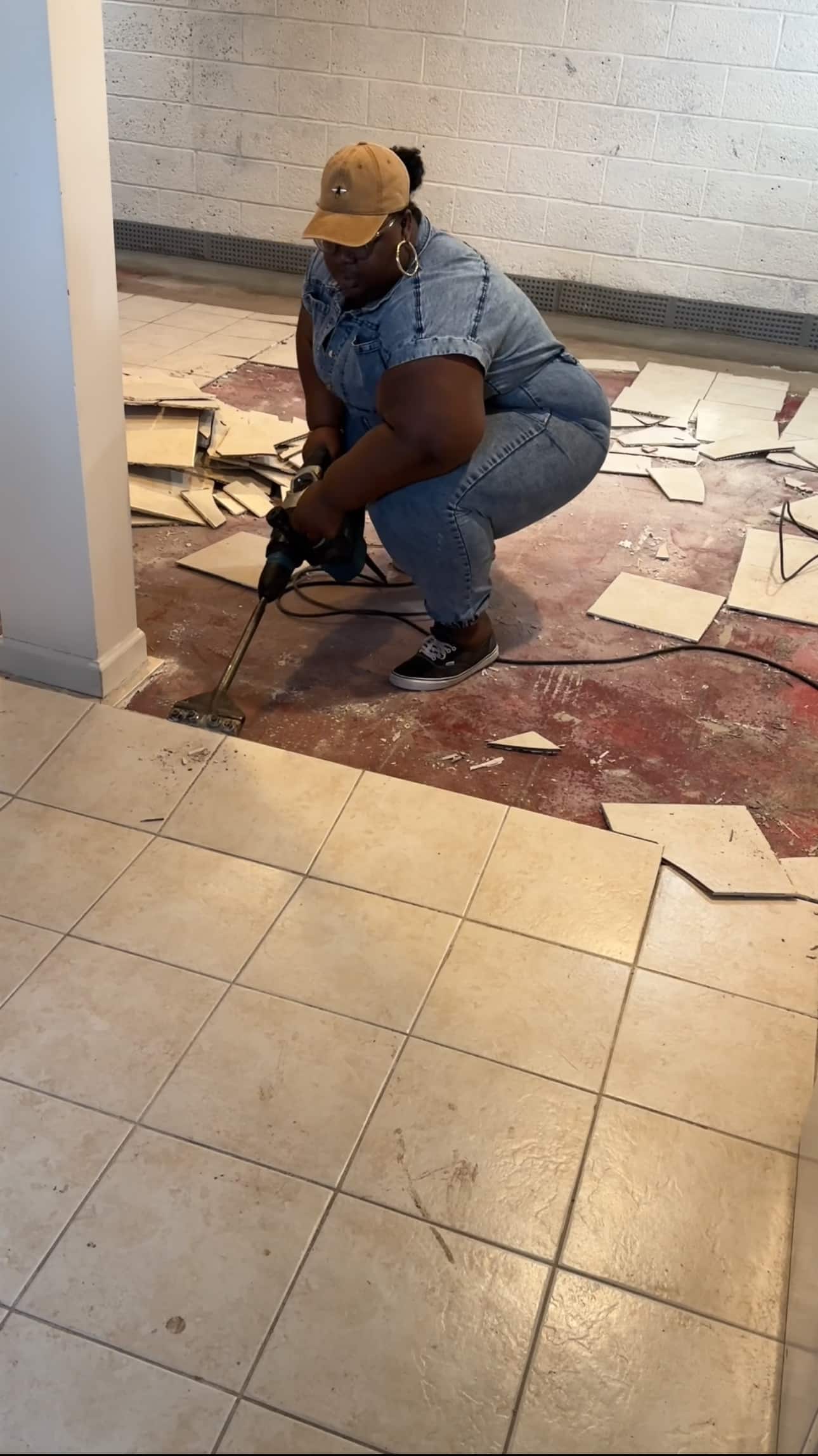 A woman using a floor scraper to remove old tiles from a basement floor.