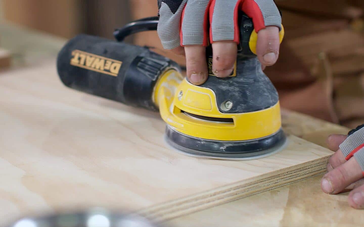 A person using a random orbital sander to smooth a DIY desk's wood.