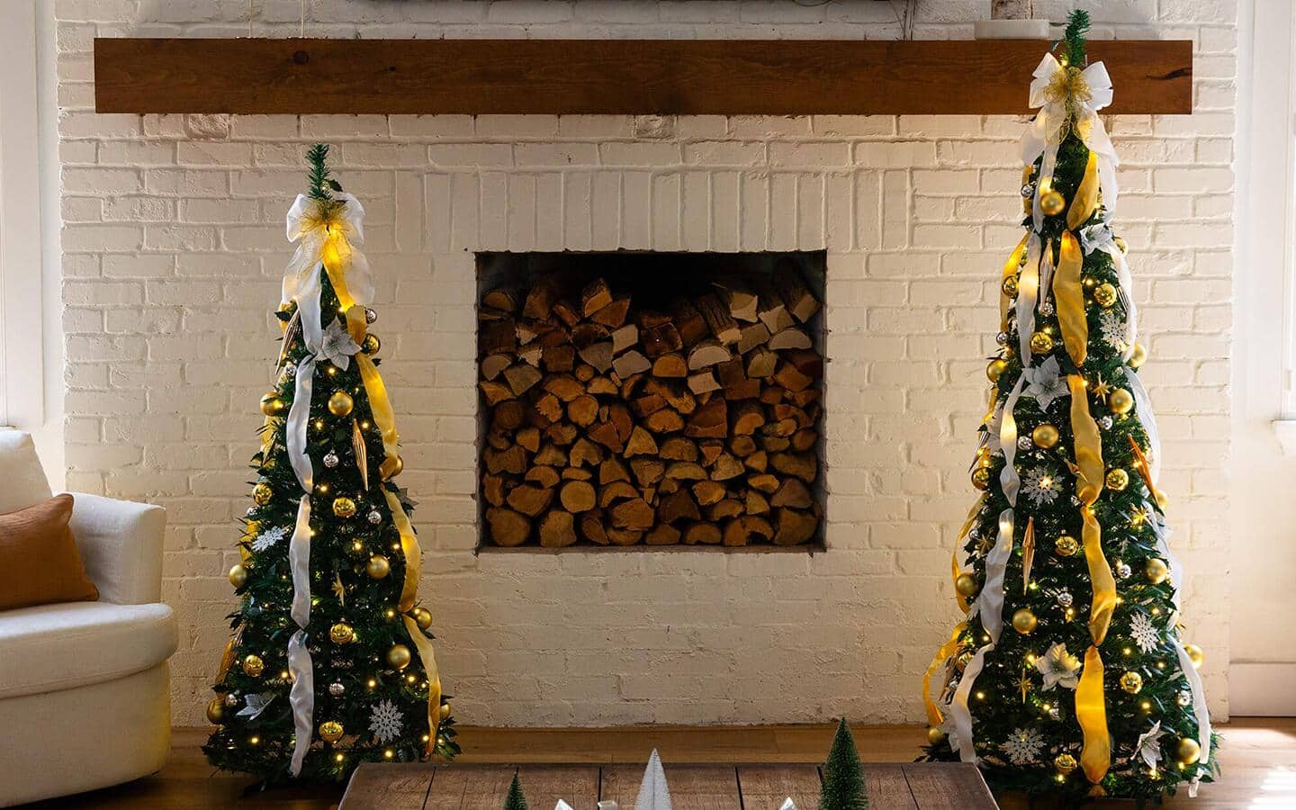 Two Christmas trees decorated with ornaments, lights and gold ribbon in a living room.