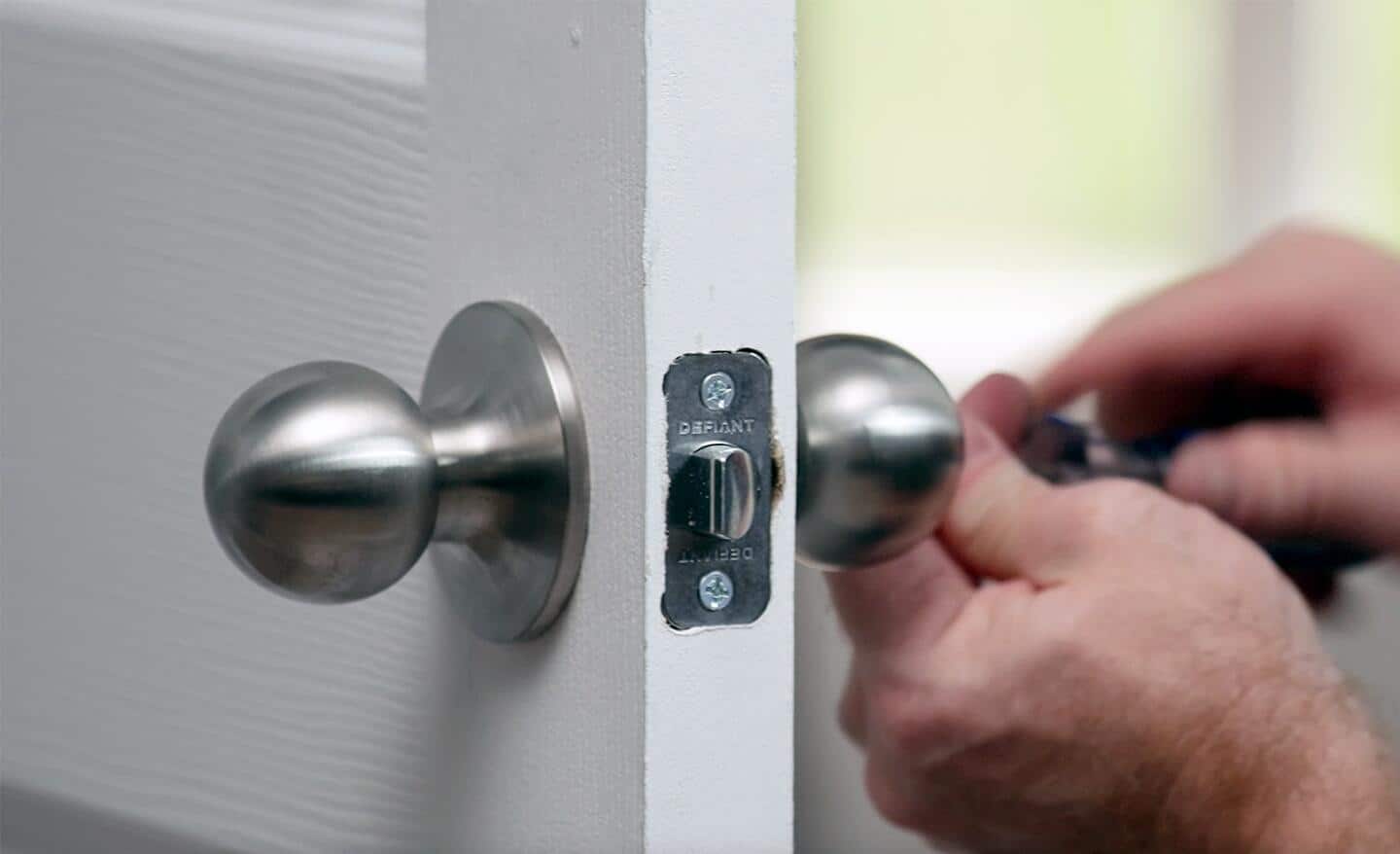 A person attaching a doorknob to an interior door.