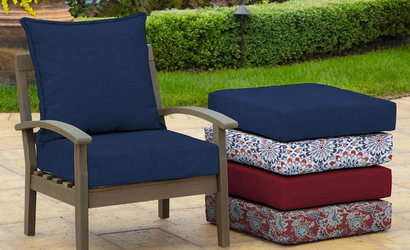 Four different colored and patterned fabric cushions stacked next to an outdoor chair with navy blue cushions.