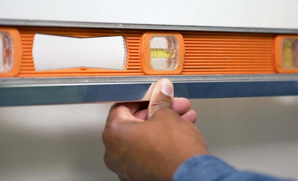 A person using a level to check measurements for a towel bar. A person using a level to check measurements for a towel bar.
