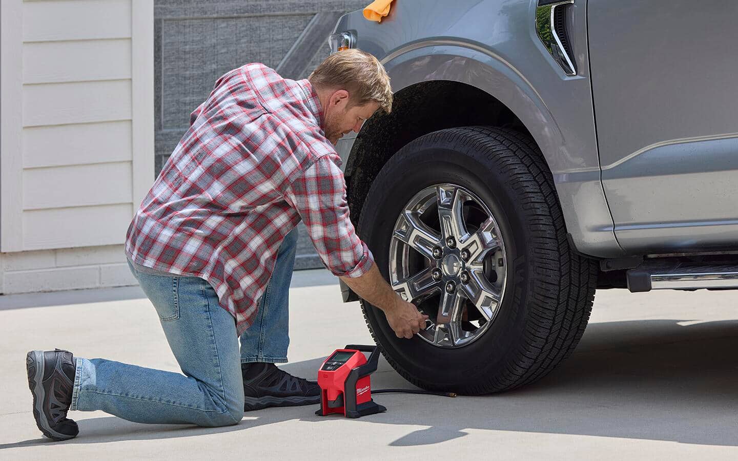 A man inflates a truck tire with a tool battery powered portable tire inflator. A man inflates a truck tire with a tool battery powered portable tire inflator.