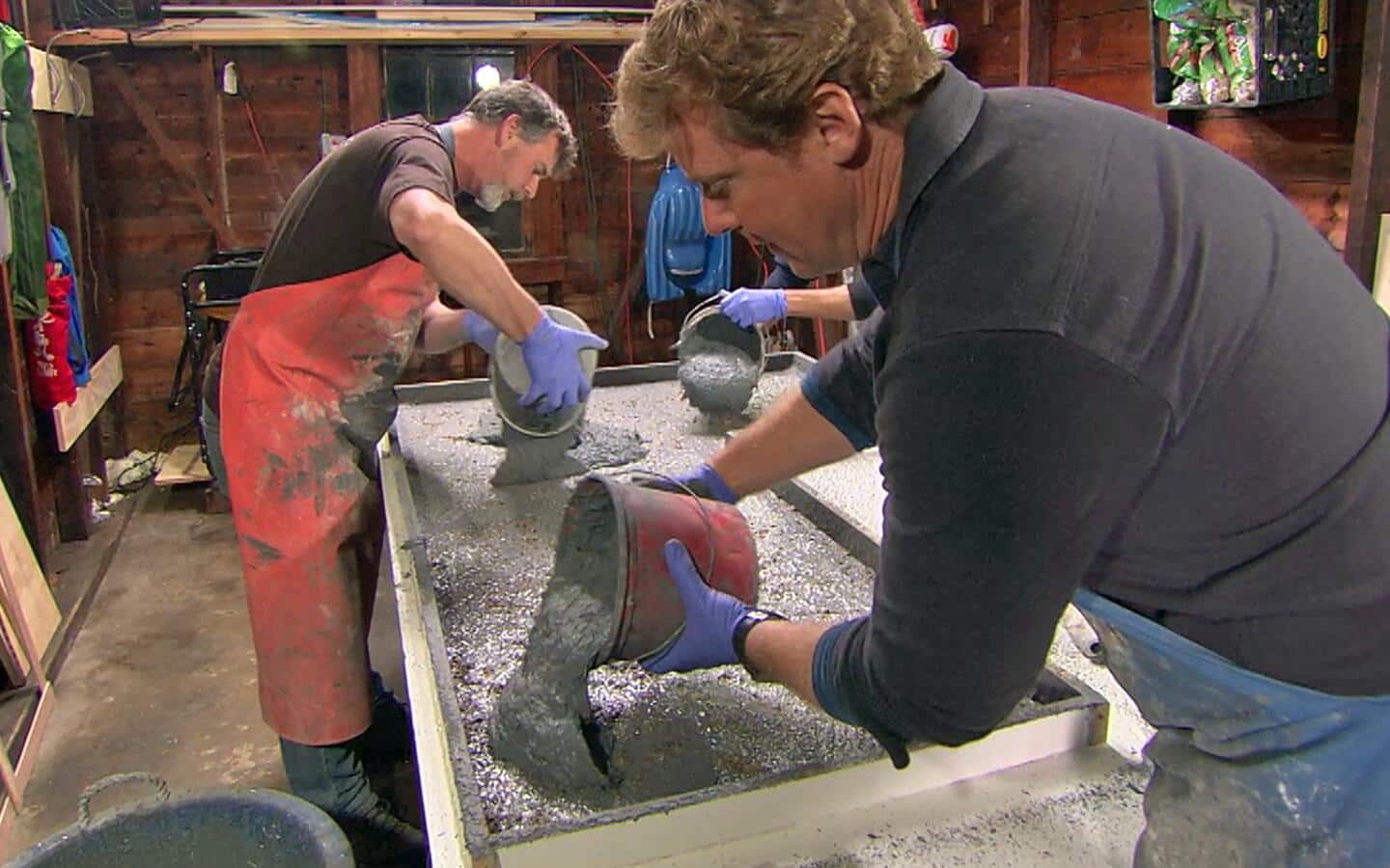 Two people scoop concrete mix into a form. Two people scoop concrete mix into a form.