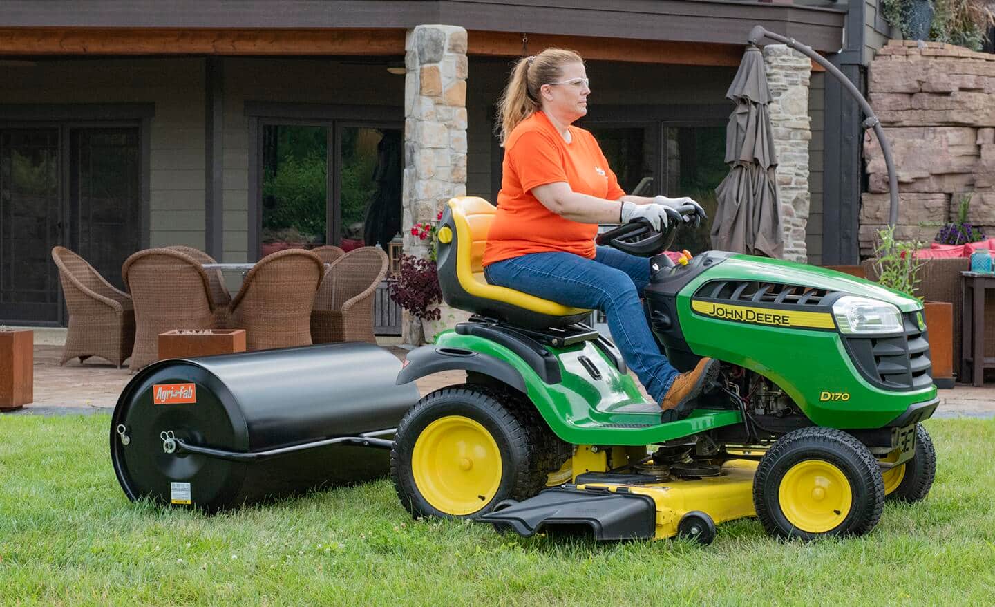 A woman riding a lawn mower with an attachment that helps bag lawn clippings.