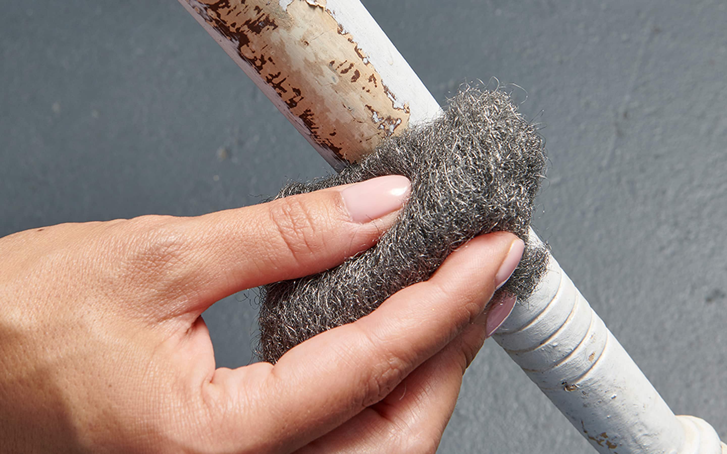Someone using steel wool to remove paint on a chair leg.