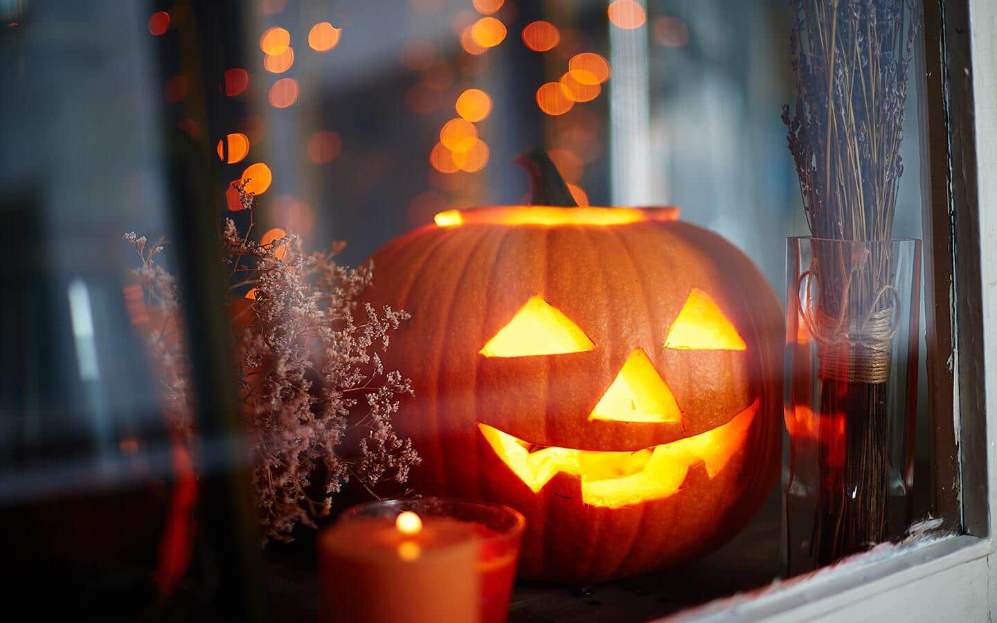 A glowing Jack-o'-lantern next to a candle in a window.