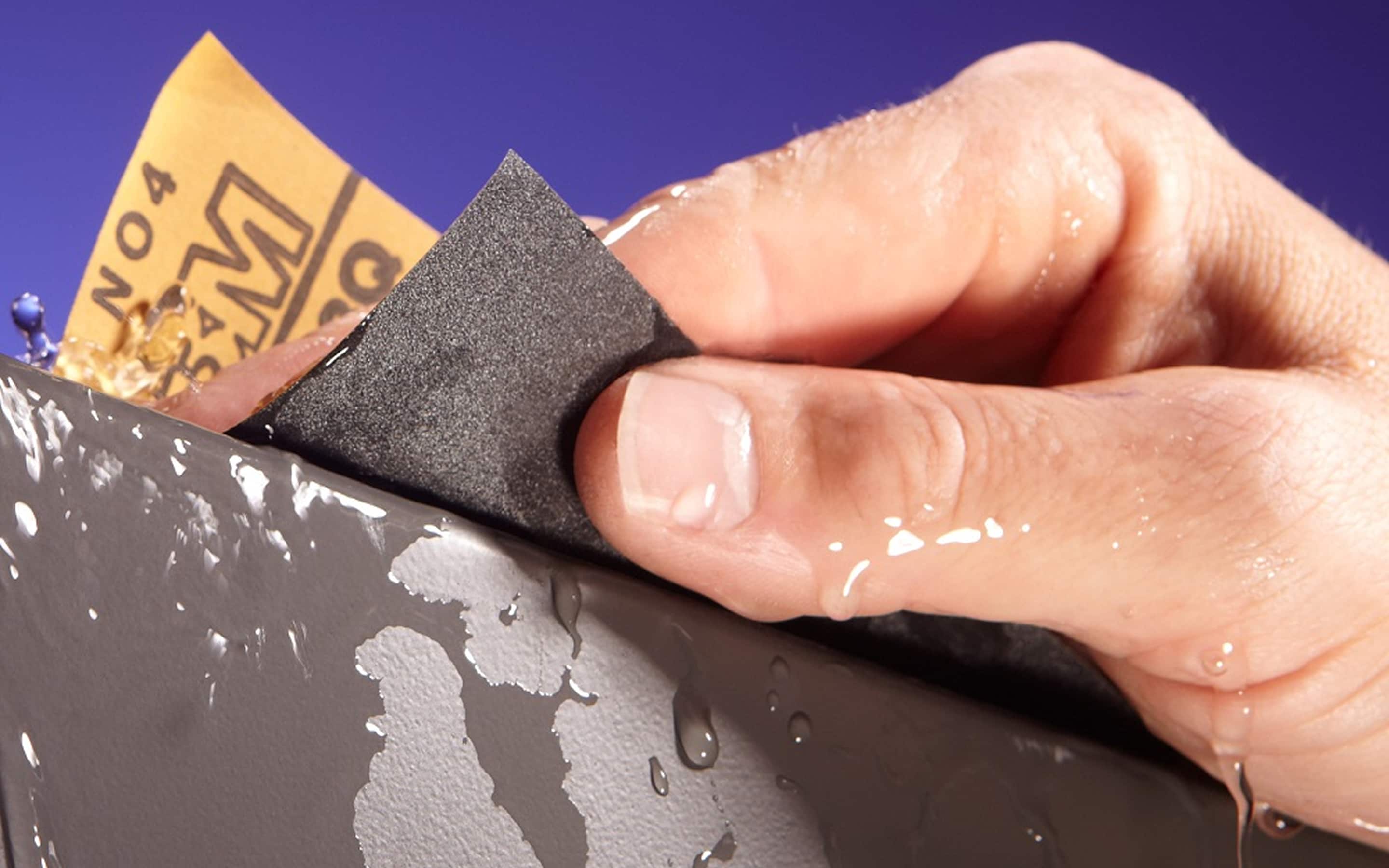 Silicon carbide sandpaper being used to sand a metal surface.