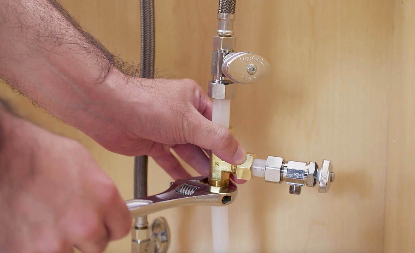 A person tapping a sink water supply to install a refrigerator water line.